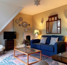 A living room with a blue sofa two patterned lamps a glass coffee table and a white armchair at Haslington House in Malvern
