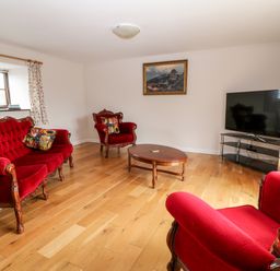 A living room with red velvet sofa chairs wooden coffee table and a television at Honeysuckle Cottage in Ashwater near Holsworthy