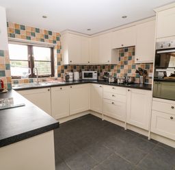 A kitchen with white cabinets black countertops tiled walls and various kitchen appliances at Honeysuckle Cottage in Ashwater near Holsworthy