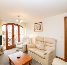 A living room with beige leather sofas a wooden coffee table a lamp a television and wooden arched doors at The Hayloft in Milton near Brampton