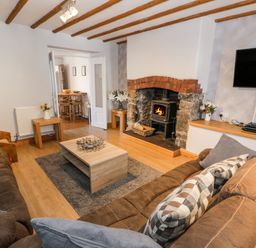 A living room with brown sofas a wooden coffee table a fireplace with fire a wall mounted tv and wooden beams on the ceiling at Tryfan in Llanberis