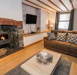 A living room with a brown sofa and checkered pillows a wooden coffee table and a fireplace with a wood stove at Tryfan in Llanberis