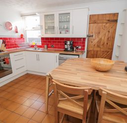 A kitchen with wooden table and chairs red tiled backsplash and wooden door at Tryfan in Llanberis