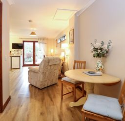 A living area with a wooden table and two chairs a vase of flowers an armchair and glass doors to the outside at Kingfisher Wattisfield near Rickinghall and Diss