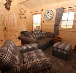 A small living room with plaid upholstered armchairs a gray sofa ottoman wooden walls and a window at The Shooting Lodge in Longnor
