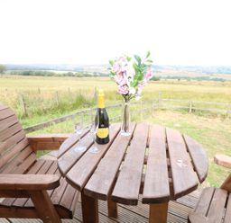 A wooden table with a bottle of prosecco two glasses and a vase of flowers on a wooden deck with a field view at The Shooting Lodge in Longnor