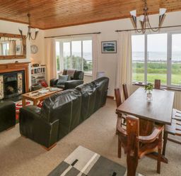 A living room with black leather sofas a wooden dining table with chairs and a fireplace at Seaspray in Tully County Galway