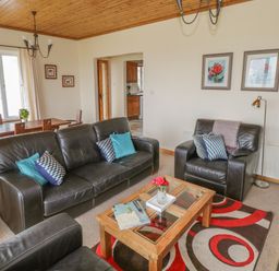 A living room with black leather sofas a wooden coffee table with books and flowers a dining table with chairs and framed artwork on the walls at Seaspray in Tully County Galway
