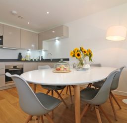 A kitchen and dining area with a white oval table surrounded by gray chairs and sunflowers in a vase at Saltwater One Lusty Glaze in Newquay