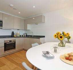 A kitchen with beige cabinets a white dining table with flowers and food at Saltwater One Lusty Glaze in Newquay