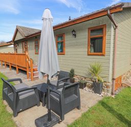 An outdoor seating area with black chairs a table and a closed umbrella next to a green house with wooden windows at Heddwch Wisemans Bridge near Saundersfoot