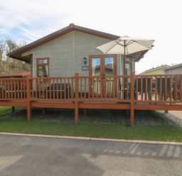 A single story cabin with a wooden deck and patio umbrella at Heddwch Wisemans Bridge near Saundersfoot