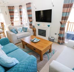 A living room with blue and beige sofas a wooden coffee table and a wall-mounted television at Heddwch Wisemans Bridge near Saundersfoot