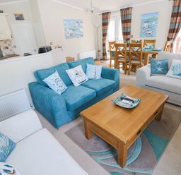 A living room with blue and white sofas and a wooden coffee table next to a dining area with wooden chairs at Heddwch Wisemans Bridge near Saundersfoot