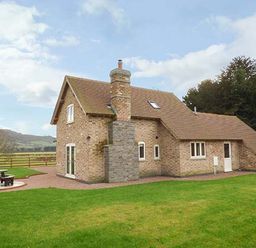 A brick house with a chimney and a picnic table in a grassy yard at Rose Cottage in Winforton near Hay-on-Wye