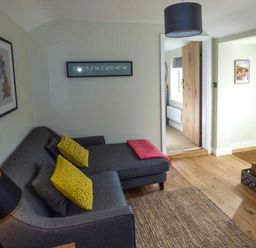 A living room with a gray sofa with yellow cushions a black lamp a rug and wooden floor at Kitts Cottage in Little Malvern near Malvern