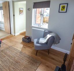 A sitting room with a gray chair and blanket a wooden floor a woven rug and a television at Kitts Cottage in Little Malvern near Malvern