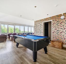 A game room with a pool table a wicker basket several armchairs and large windows at The Oaks in Bowness & Windermere