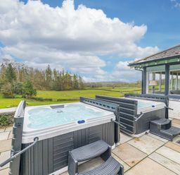 An outdoor patio with two hot tubs and steps overlooking a grassy field and trees at The Oaks in Bowness Windermere