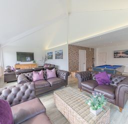 A living room with brown leather sofas purple cushions a wicker coffee table a flat screen tv and a pool table at The Oaks in Bowness & Windermere