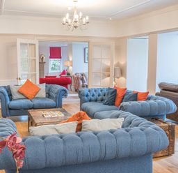 A living room with blue sofas orange cushions and a chandelier at The Oaks in Bowness & Windermere
