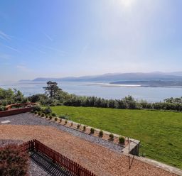 A garden with grass and shrubs overlooking a body of water with hills in the background at Menai View near Menai Bridge