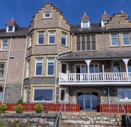 The exterior of a multi-story stone house with multiple windows a balcony and a red wooden fence near Menai Bridge