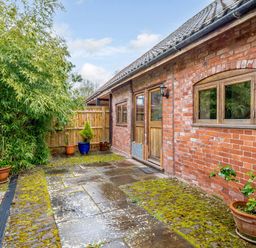 An outdoor patio area with stone paving and moss next to a brick building with wooden doors and windows at The Bothy in Phocle Green near Ross-on-Wye