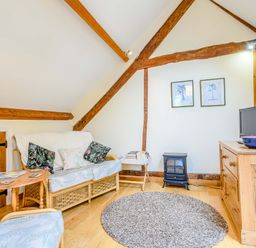 A living room with wicker furniture a small wooden table a gray round rug a wooden dresser with a TV and two framed pictures on the wall at The Bothy in Phocle Green near Ross-on-Wye