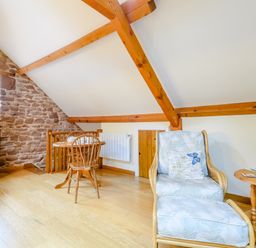 An attic room with wooden beams a small dining table and chair a cushioned armchair with footstool and a side table at The Bothy in Phocle Green near Ross-on-Wye