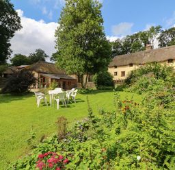 A garden with plastic chairs and a table on grass near plants and houses with thatched roofs at The Milking Parlour in Highampton