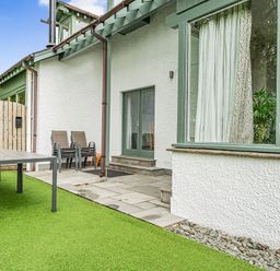An outdoor area with a table, stacked chairs, a wooden gate, and a green grassy surface at Beech - Woodland Cottages in Bowness-on-Windermere