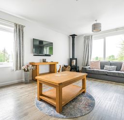 A living room with a wooden coffee table a grey sofa a wall-mounted tv and a stove at Beech - Woodland Cottages in Bowness-on-Windermere