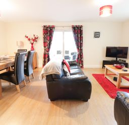 A living room with black leather sofas a wooden dining table with black chairs a coffee table a television and red and black curtains at Arnant in Barmouth