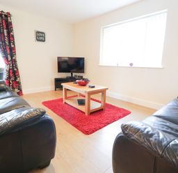 A living room with two black leather sofas a wooden coffee table on a red rug a wall mounted TV and floral curtains at Arnant in Barmouth