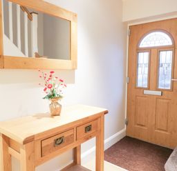An entryway with a wooden door a wooden table with drawers a vase with flowers and a wall mirror at Arnant in Barmouth