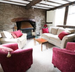 A sitting room with two beige sofas two red armchairs a wooden coffee table and a stone fireplace at Causeway Cottage in Pencombe
