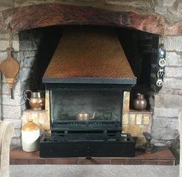 A stone fireplace with a copper hood and various metal pots and a wood bellows at Causeway Cottage in Pencombe