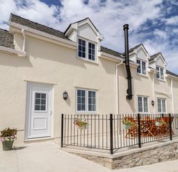 The exterior of a cream-colored house with a patio, wooden furniture, and hanging flower pots at Delfryn in Llannefydd near Denbigh
