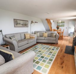 A living room with three sofas and a patterned rug near a dining table and wood stove at Delfryn in Llannefydd near Denbigh