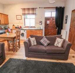 An open-plan kitchen and living area with wooden cabinets a dining table two sofas and a wooden door at The Old School Room in Longhorsley near Morpeth and Alnwick