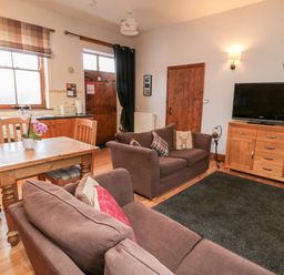 A living room with brown sofas a wooden table and chairs a television on a wooden cabinet and windows at The Old School Room in Longhorsley near Morpeth and Alnwick