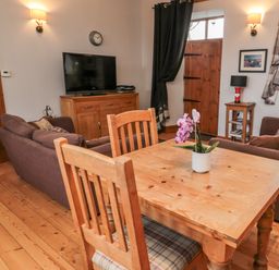 A living room with a wooden dining table and chairs a television on a wooden cabinet and sofas at The Old School Room in Longhorsley near Morpeth and Alnwick