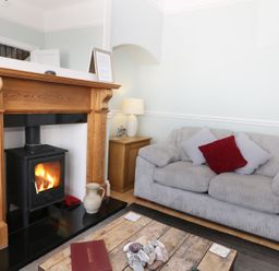 A living room with a wood burning stove fireplace a grey sofa with cushions a wooden coffee table and a side table with a lamp at Number Fifteen in Withernsea