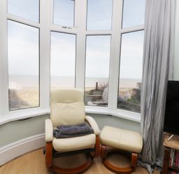 A cream chair with an ottoman in front of bay windows overlooking the sea at Number Fifteen in Withernsea