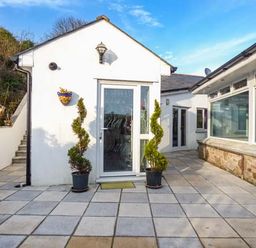 An outdoor patio area with tiled flooring two spiral-shaped potted plants a white building with glass doors and windows at Chapel Green Studio Polgooth near St Austell