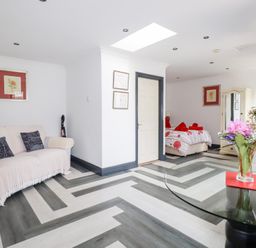 A room with a sofa, a bed, a glass table with flowers, and a wall-mounted television at Chapel Green Studio in Polgooth near St Austell