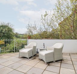 An outdoor patio with two white armchairs a small round table and potted plants at Chapel Green Studio Polgooth near St Austell