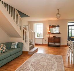 A living room with a green sofa near stairs a wooden sideboard under a mirror and a dining table with chairs at Ballintlea in Ballintlea near Dungarvan County Waterford