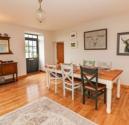 A dining room with a wooden table and mixed chairs a sideboard with a mirror and decorative plates on top and animal artwork on the walls at Ballintlea near Dungarvan County Waterford